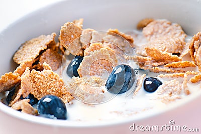 Full muesli bowl on a white table with blueberry and milk splash. Healthy breakfast cereals with milk, seed, fruit. Oat flakes Stock Photo