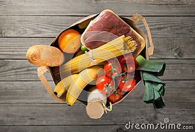 Full paper bag of different groceries on wooden background Stock Photo
