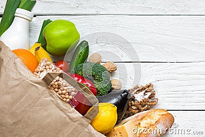 Full paper bag of different healthy vegetarian food on white wooden background. fruits, vegetables, nuts, bread and milk Stock Photo