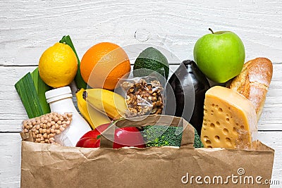 Full paper bag of different healthy vegetarian food on white wooden background Stock Photo