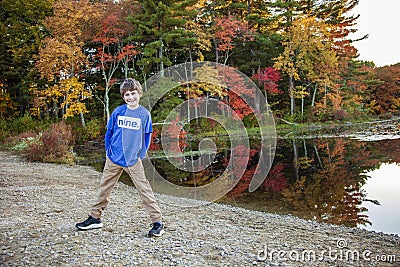 Full portrait of a smiling nine year old boy outside by a lake with colorful fall trees Stock Photo