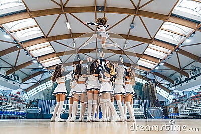 Full shot of a cheerleading squad hrowin one of their teammates high up in the air. Sport concept. Stock Photo