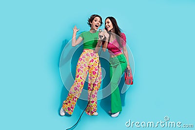 Full size body photo of two singing drunk girlfriends weekend karaoke discotheque hold boombox player isolated on blue Stock Photo