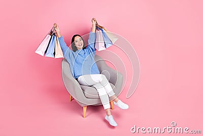 Full size photo of funny woman wear knit pullover trousers raising shopping bags sit on armchair on pink color Stock Photo