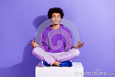 Full size photo of peaceful relaxed person wear stylish pullover sit on cube in meditation pose isolated on purple color Stock Photo