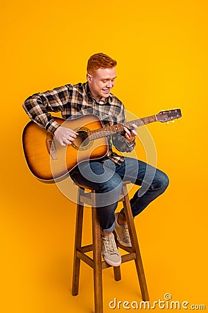 Full size photo of young handsome man sit stool play guitar performance stage isolated over yellow color background Stock Photo