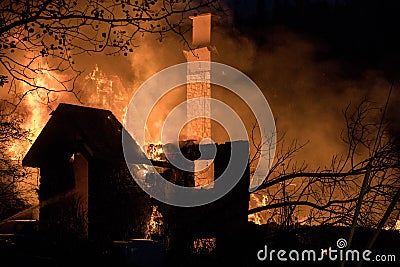 Fully engulfed house fire. Chimney stand in middle of the debris. Stock Photo