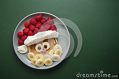 Winter food for kids. Christmas Santa pancake with raspberry and banana for children menu, green background, copy space Stock Photo