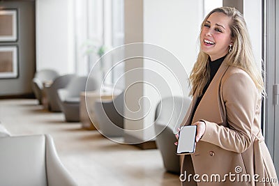 Fun, friendly, fashionable smiling business person in modern luxury office space lobby holding smartphone Stock Photo