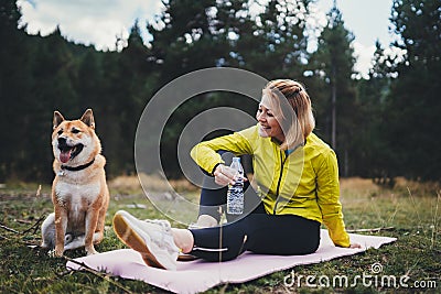 Fun girl with pet together relax after exercising outdoors on yoga mat, shiba inu dog on nature fitness woman drink water Stock Photo