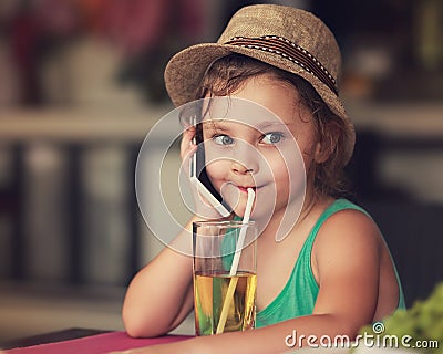 Fun happy kid girl talking on mobile phone and drinking apple juice in cafe. Toned closeup portrait Stock Photo
