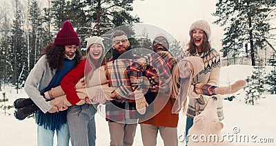 Fun happy multiethnic friends hold, rock young blonde woman laughing at snowy forest Christmas vacation slow motion. Stock Photo