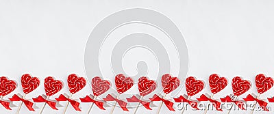 Fun valentines day background - sweet red lollipops hearts with bows on white wood board as decorative seamless border for banner. Stock Photo