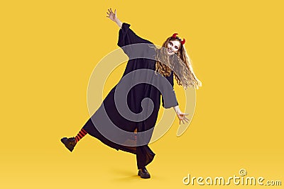 Funky woman in halloween costume, terrifying makeup, red devil horns dancing on yellow background. Stock Photo