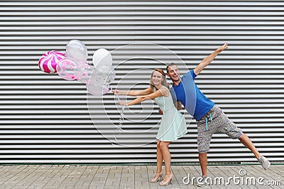 Funky young couple holding balloons while jumping against striped background Stock Photo