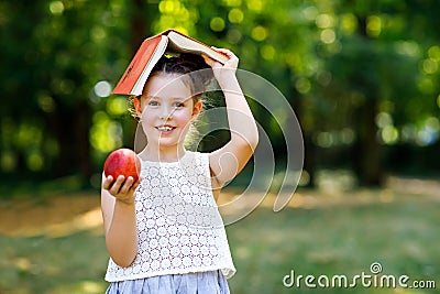 Funny adorable little kid girl with book, apple and backpack on first day to school or nursery. Child outdoors on warm Stock Photo