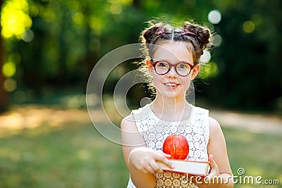 Funny adorable little kid girl with glasses, book, apple and backpack on first day to school or nursery. Child outdoors Stock Photo