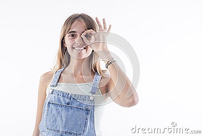 Funny amusing blonde girl in jeans dress showing okay gesture near her eye Stock Photo