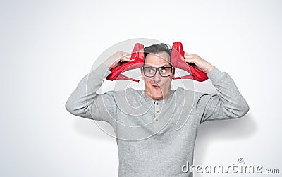 A funny and amusing man with glasses holding female red high-heeled shoes near his head in both hands Stock Photo