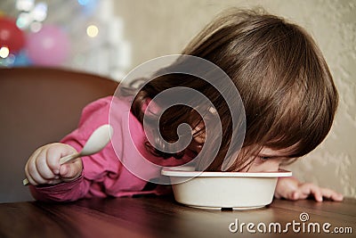 Funny baby eats porridge with spoon Stock Photo