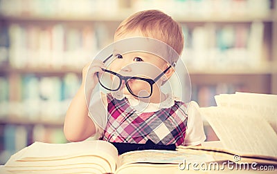 Funny baby girl in glasses reading a book in a library Stock Photo