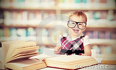 Funny baby girl in glasses reading book in library Stock Photo