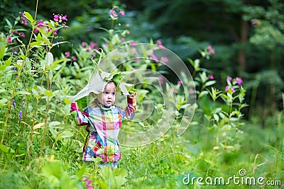 Funny baby girl playing peek a boo in a park under huge leaves Stock Photo
