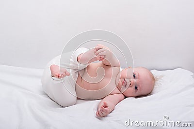 Funny baby lying down on white sheet. Newborn lying on side and smiling Stock Photo