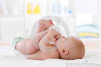 Funny baby wearing diaper. Infant kid skin care. Cute child playing with his feet Stock Photo