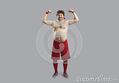 Happy topless man in sports shorts with some belly fat flexing arms showing his muscles Stock Photo