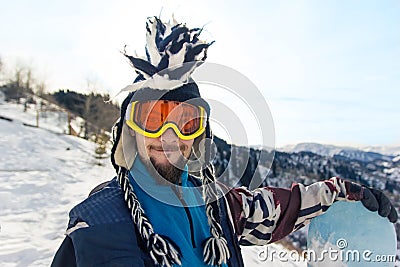 Funny bearded man snowboarder portrait in mohawk hat enjoys the ski resort in the mountains Stock Photo