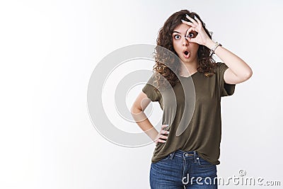 Funny carefree cute armenian young woman curly-haired say wow widen eyes surprised amused show okay gesture on eye look Stock Photo