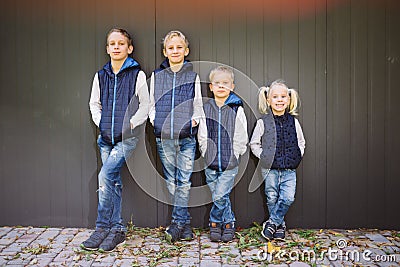 Funny Caucasian big family of three brothers and sister posing standing on growth background of wall in full growth. Equally Stock Photo