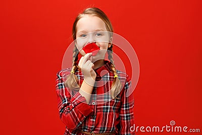 Funny cheerful little girl makes artificial fake lips on a red background. Child fooling around Stock Photo