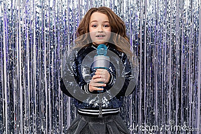 Funny cheerful stylish girl with a microphone in her hands on a shiny tinsel background Stock Photo