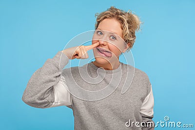 Funny cheerful woman with short hair in casual sweatshirt picking nose with stupid silly face, pulling out boogers Stock Photo