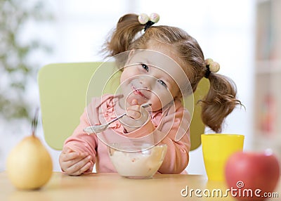 Funny child eating healthy food with a spoon at home Stock Photo