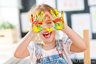 Funny child girl draws laughing shows hands dirty with paint Stock Photo