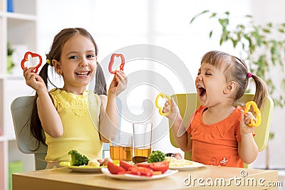 Funny children girls eating healthy food. Kids lunch at home or kindergarten. Stock Photo