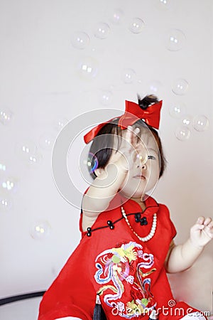 Funny Chinese little baby in red cheongsam play soap bubbles Stock Photo