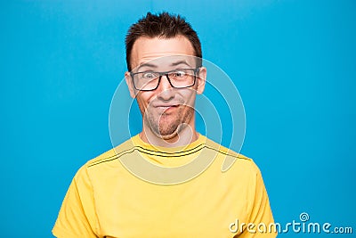 Funny comic man in glasses makes grimace with crosses eyes. Young man in yellow t-shirt with crazy expression has fun alone Stock Photo