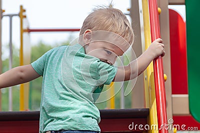 Funny cute caucasian blonde baby boy plays on the playground, climbing to upstair. Stock Photo