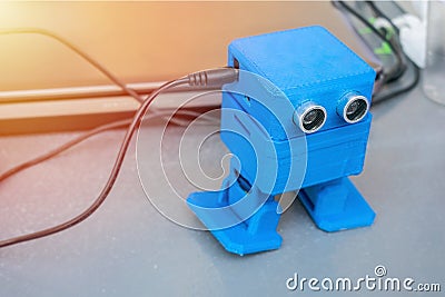 Funny dancing blue robot, printed on the 3D printer on the background of devices and cords. The robot model printed on automatic Stock Photo