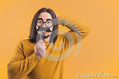Funny disguise concept. Adult caucasian man wearing fake glasses and mustache over yellow background. Stock Photo