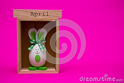 Funny egg in the form of cute bunny with wooden calendar set on april on pink background Stock Photo