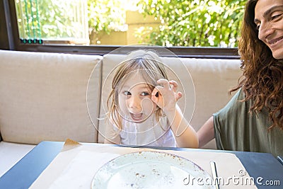 Funny girl teasing next to mother sitting in restaurant Stock Photo