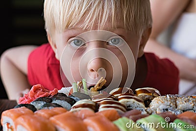 Funny fair-haired boy stares at Sushi. Child boy in cafe concept. Asian cuisine Stock Photo