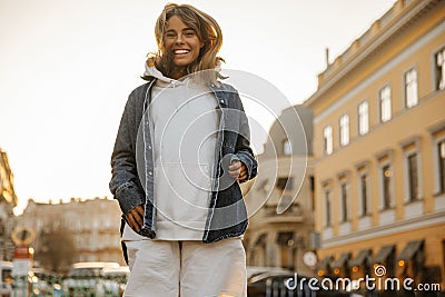 Funny fair-skinned young girl jumps on spot, smiling broadly to her teeth in city center. Stock Photo