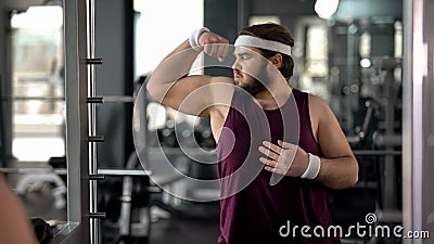 Funny fat man looking at mirror reflection gym and posing, pretending muscular Stock Photo