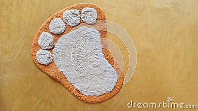 Funny fluffy rug in the shape of a foot on a beige wooden floor. Stock Photo
